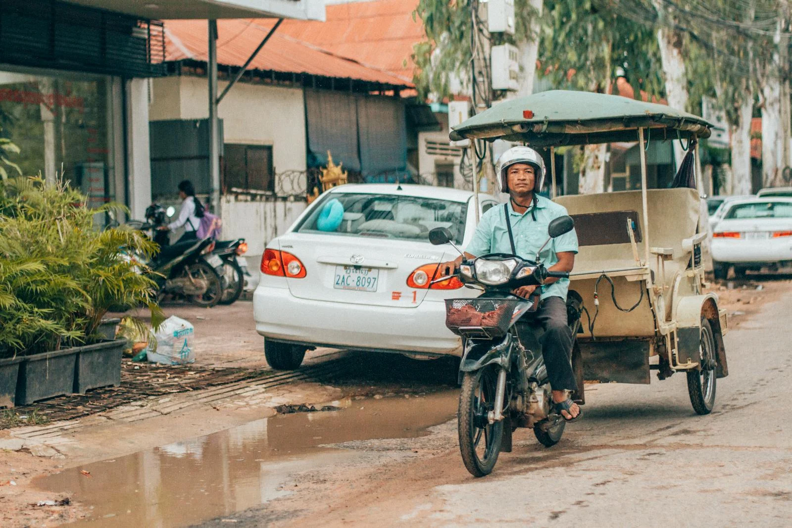 A tuk-tuk driver rides through the streets of Siem Reap, Cambodia, showcasing urban transportation.