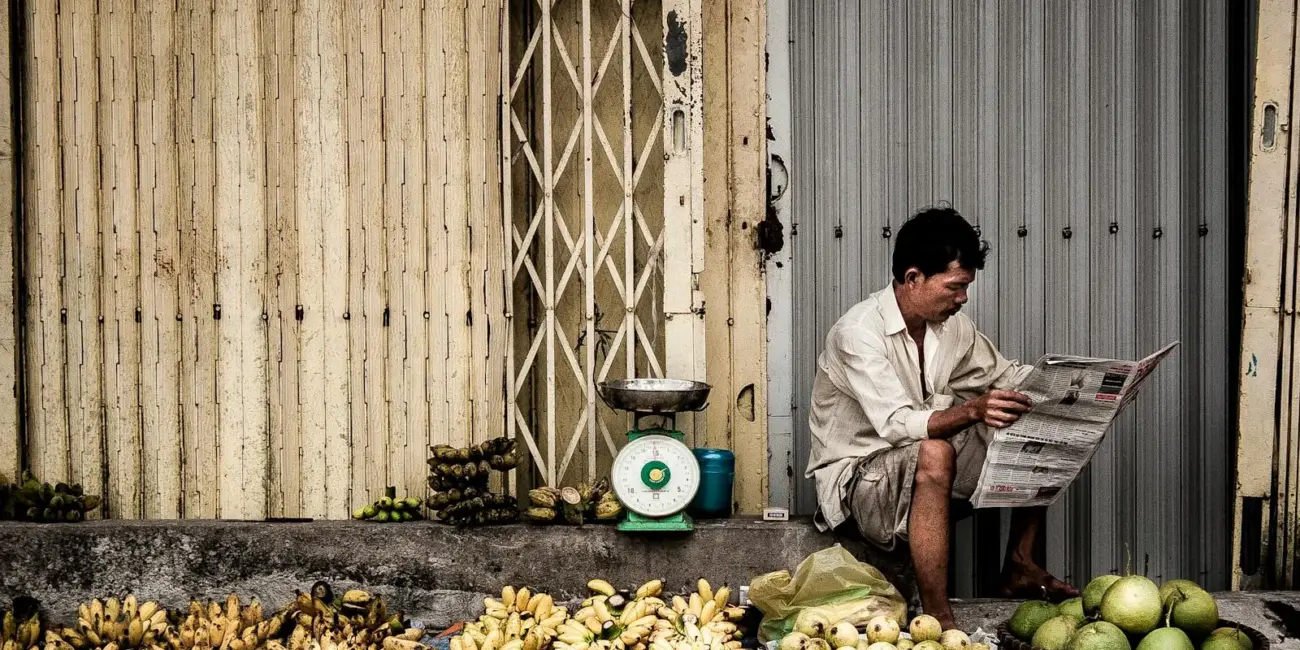 A Vietnamese vendor reads a newspaper beside fresh fruits on a street market in Ho Chi Minh City.