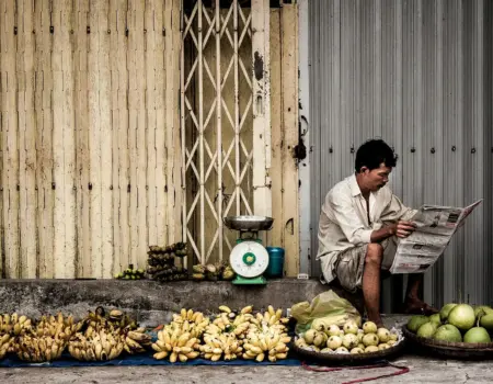 A Vietnamese vendor reads a newspaper beside fresh fruits on a street market in Ho Chi Minh City.