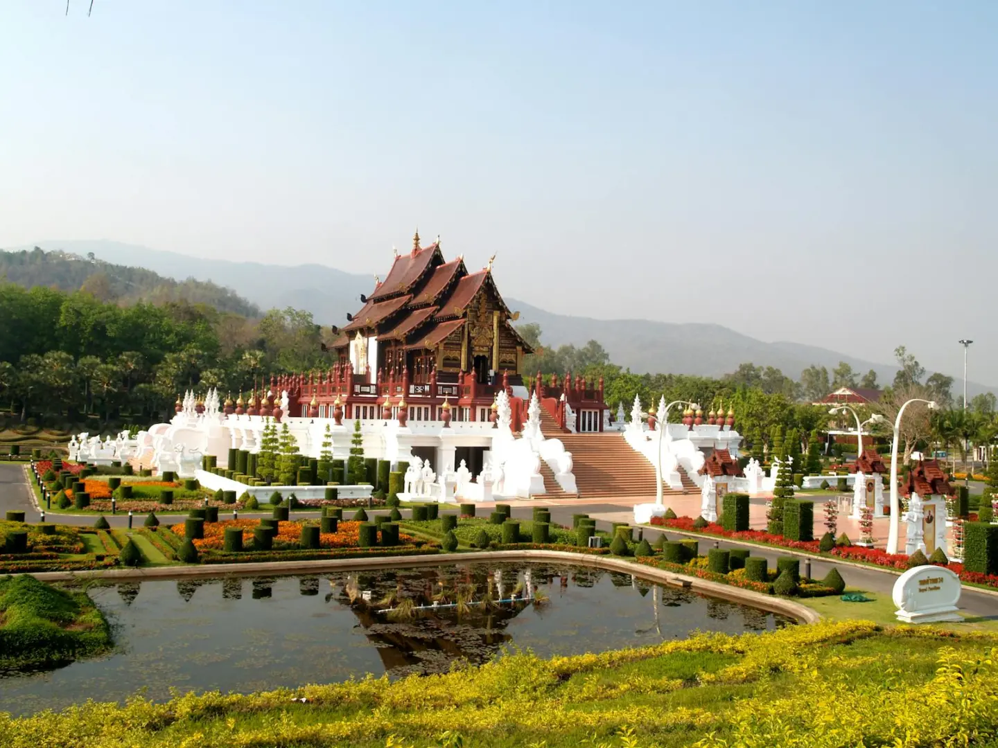 A beautiful Thai temple amidst lush gardens and a reflecting pond in daylight.