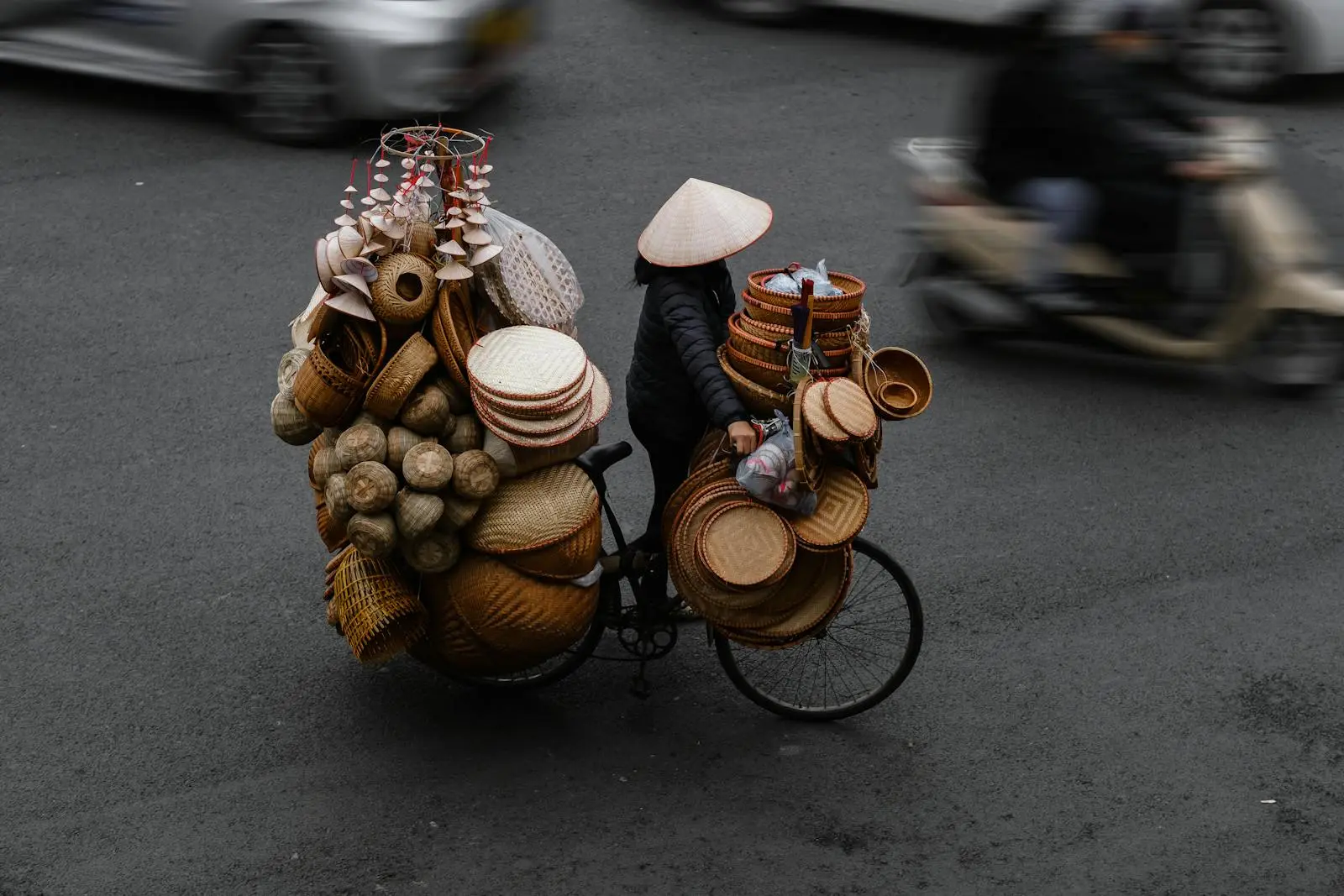 Street vendor with woven baskets on a bicycle in bustling Hanoi. Captured in motion.
