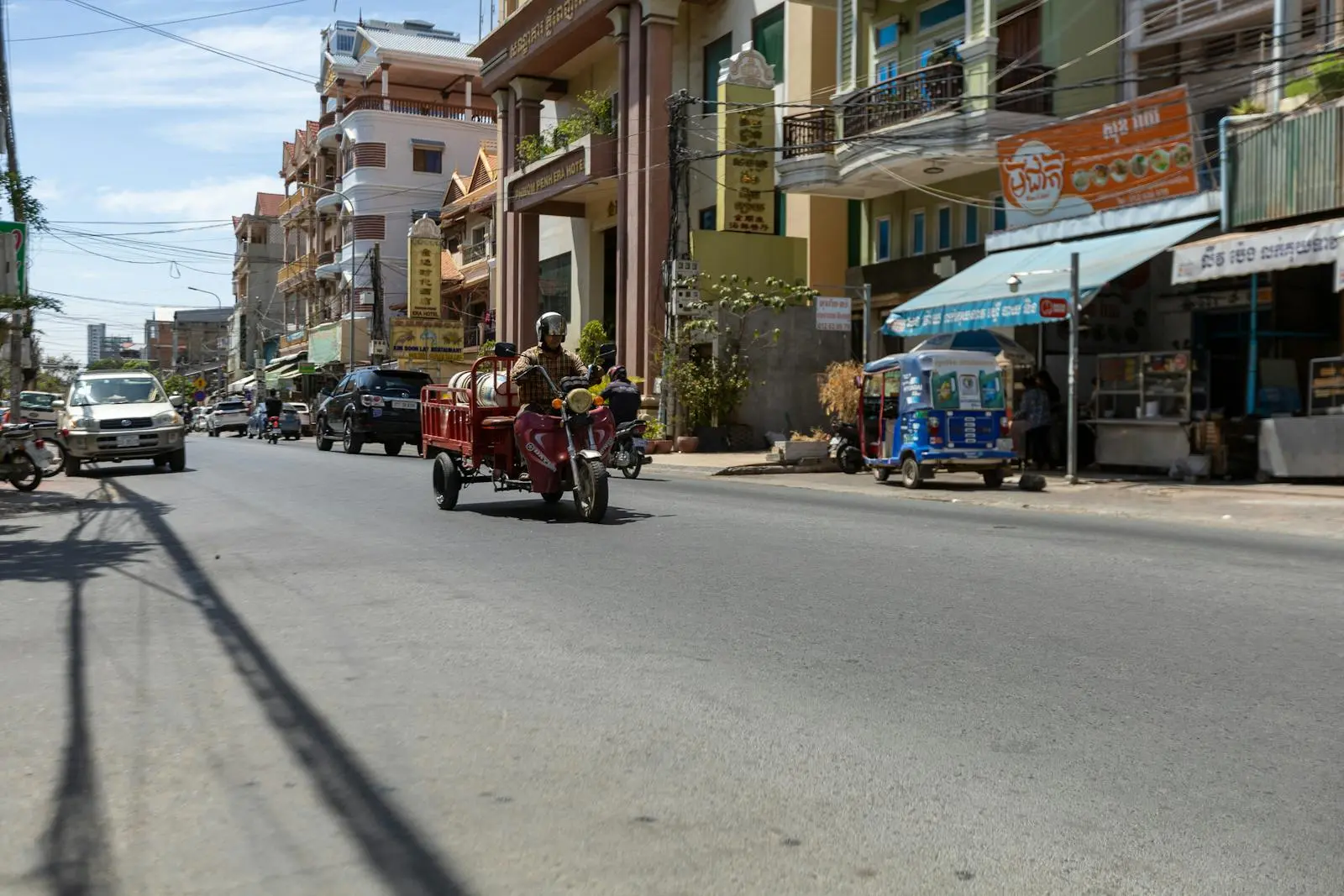 Busy Southeast Asian street with motorbike and colorful buildings on a sunny day.