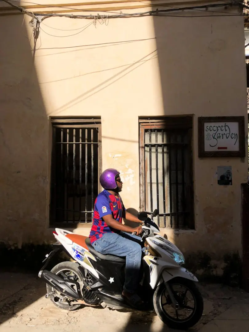 A man riding a scooter in a sunlit alley in Stone Town, Zanzibar.