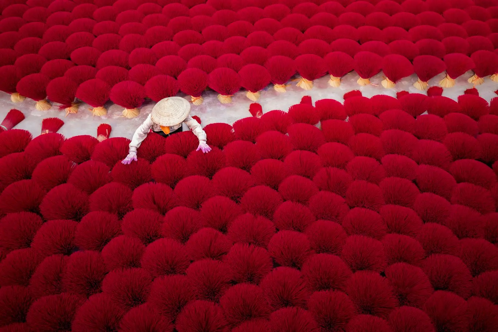 Aerial view of red incense sticks drying outdoors, worker in traditional hat.