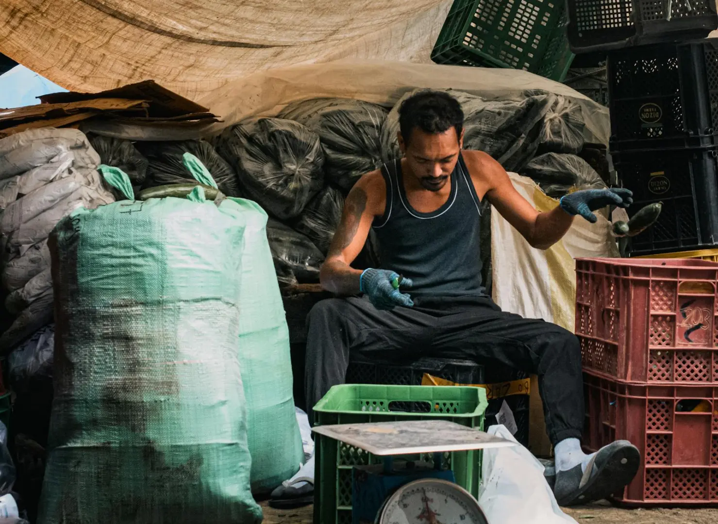 Market vendor sorting goods at Baguio City market, surrounded by crates and bags.