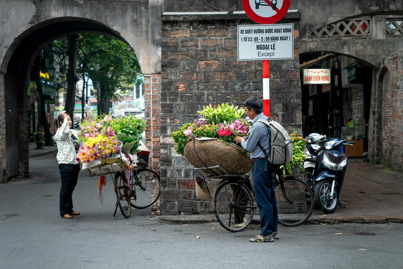 Side view of male in casual clothes standing near bicycle with baskets of colorful flowers of vendor and buying flowers from woman on town street