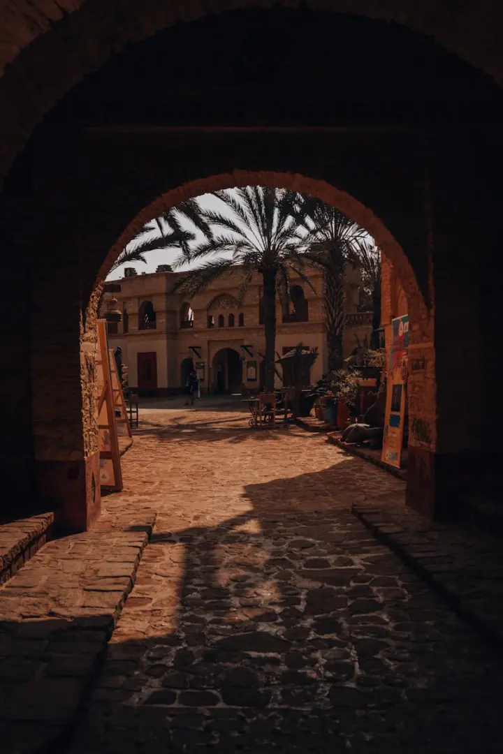 An archway frames a building with a palm tree.