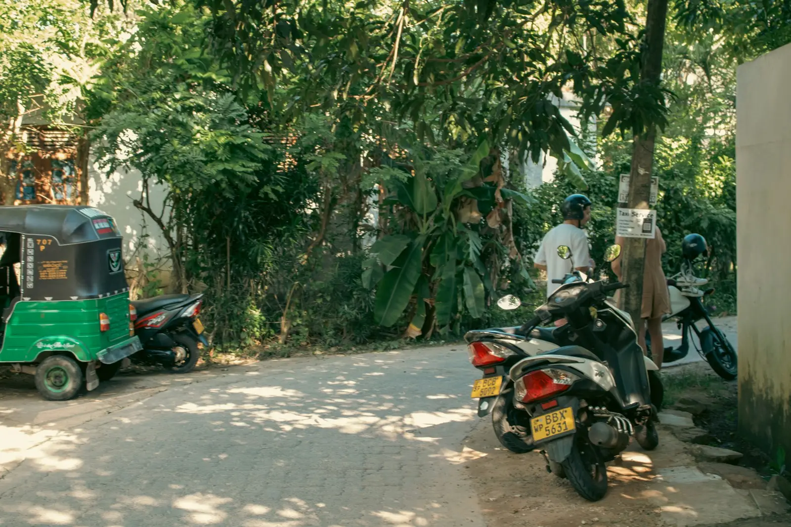 Prenájom tuk tuku na Srí Lanke 3 A green tuk-tuk and scooters parked on the street.