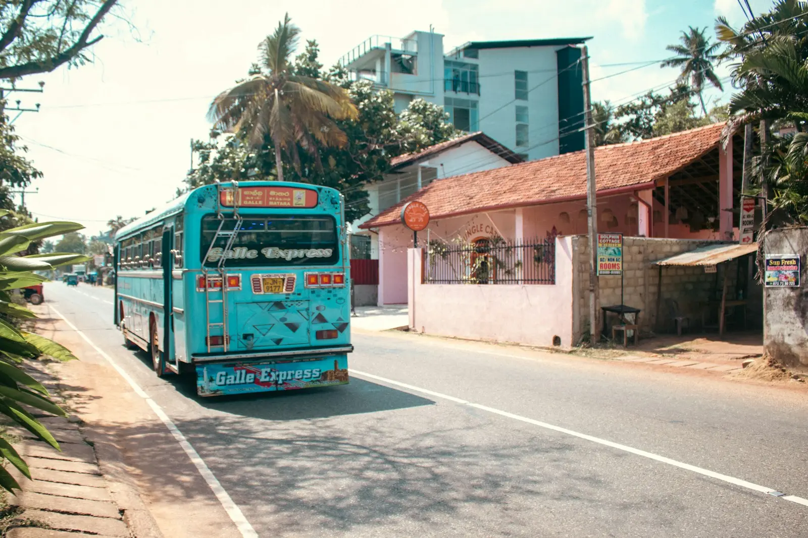 Photo by Zoshua Colah A blue bus drives down a sunny sri lankan road.
