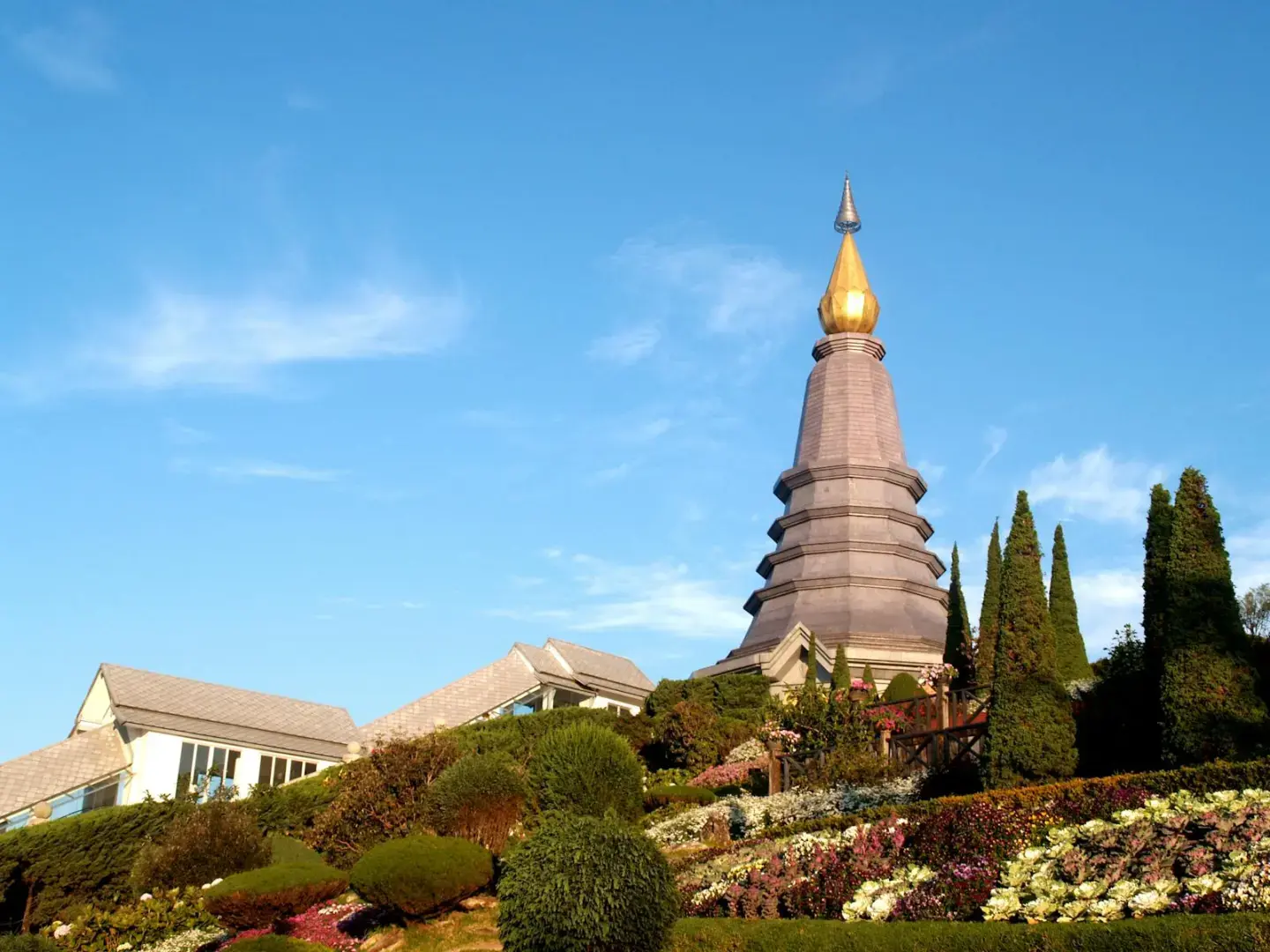 Beautiful view of a Buddhist pagoda surrounded by a vibrant garden in Chiang Mai, Thailand, under a clear blue sky.