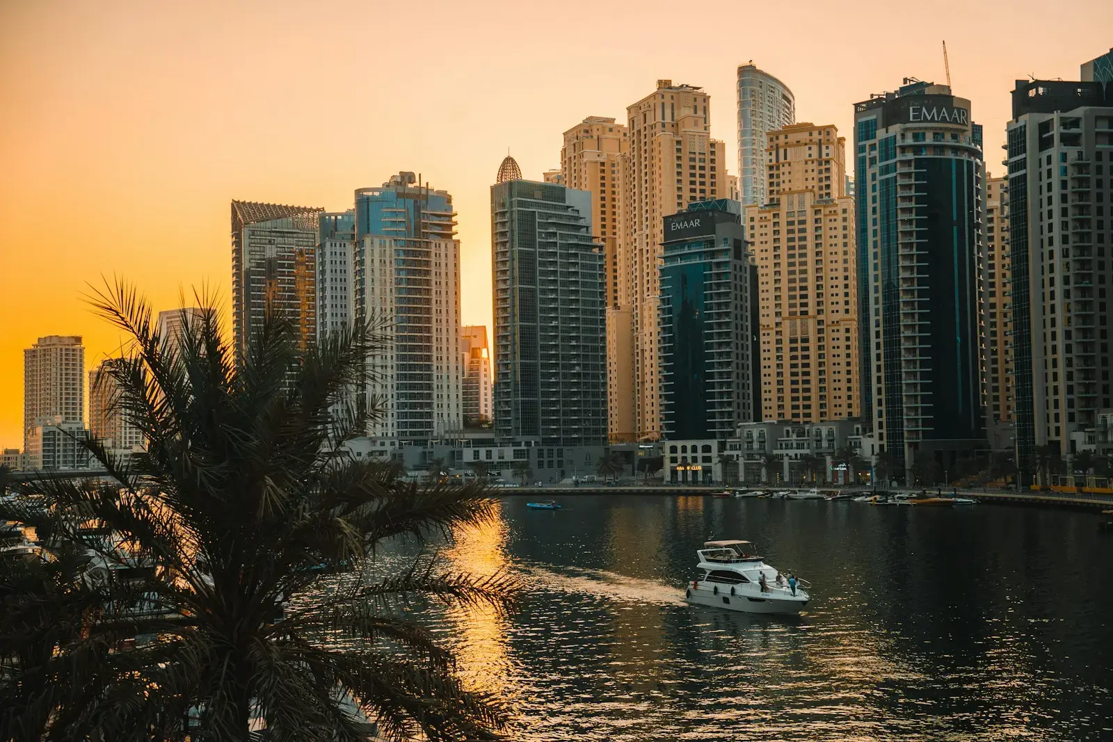 A boat sails on water with city skyscrapers at sunset.