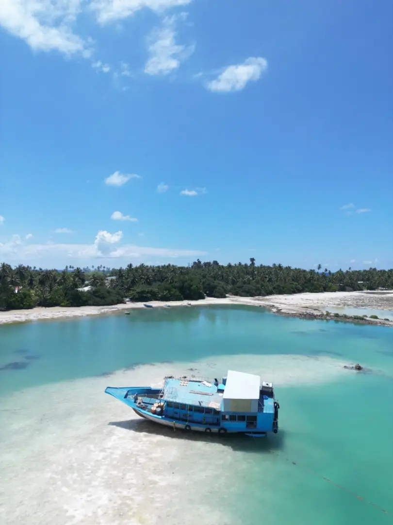 Blue boat grounded on sandy shore with tropical island background