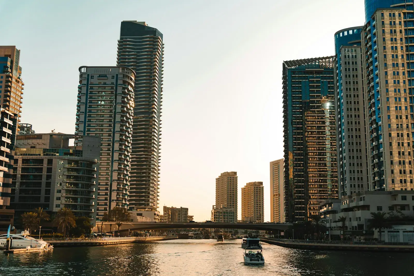 Modern skyscrapers line a calm canal with boats.