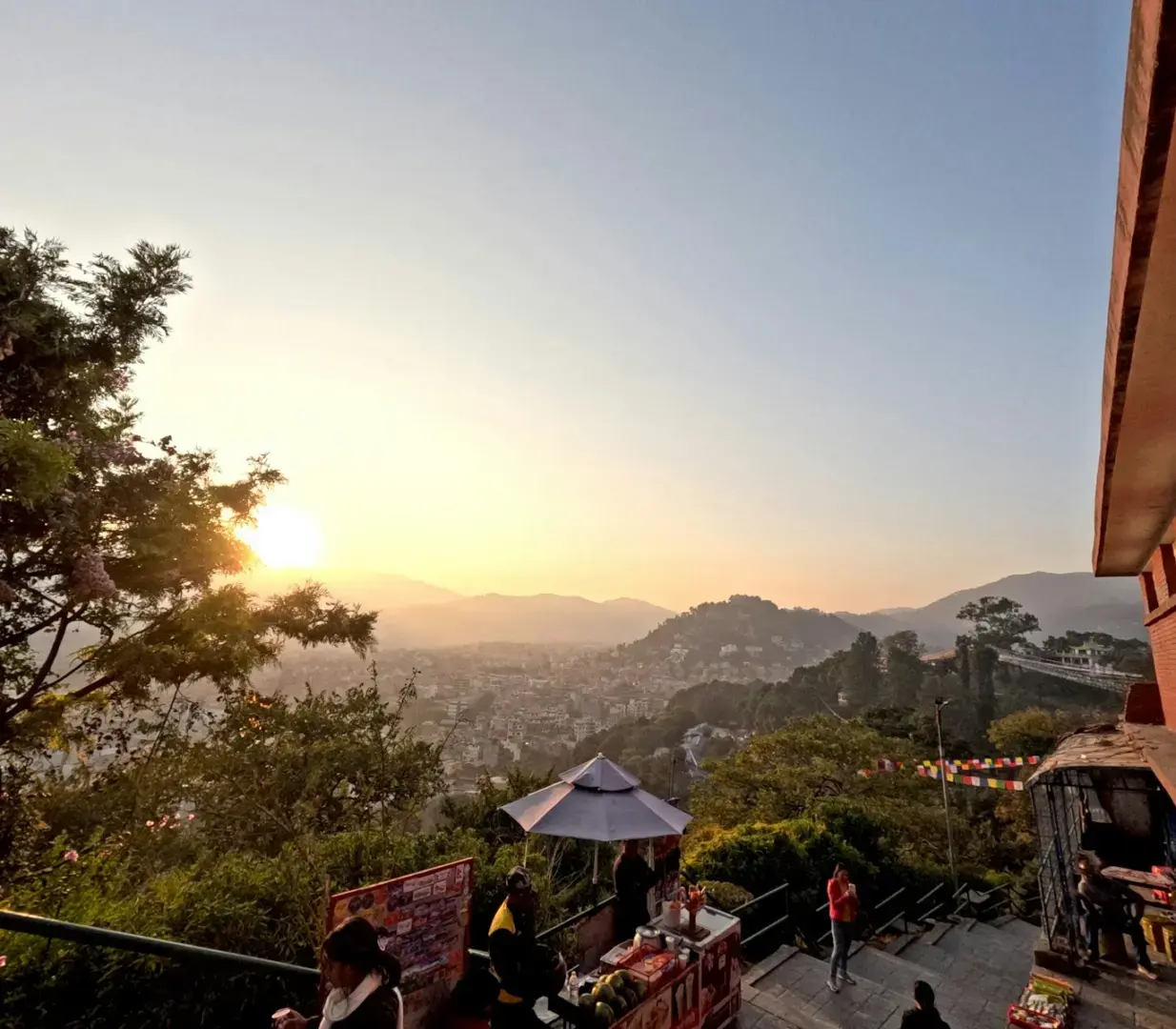 Sunset over a hilly city with trees in foreground.