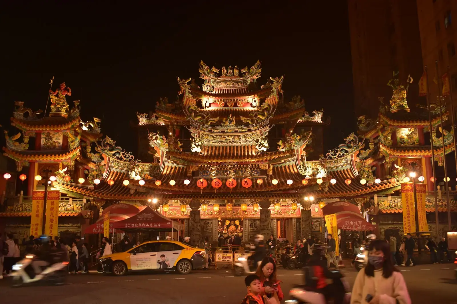 Photo by Leandro De Torres Ornate temple entrance illuminated at night with people and crowds