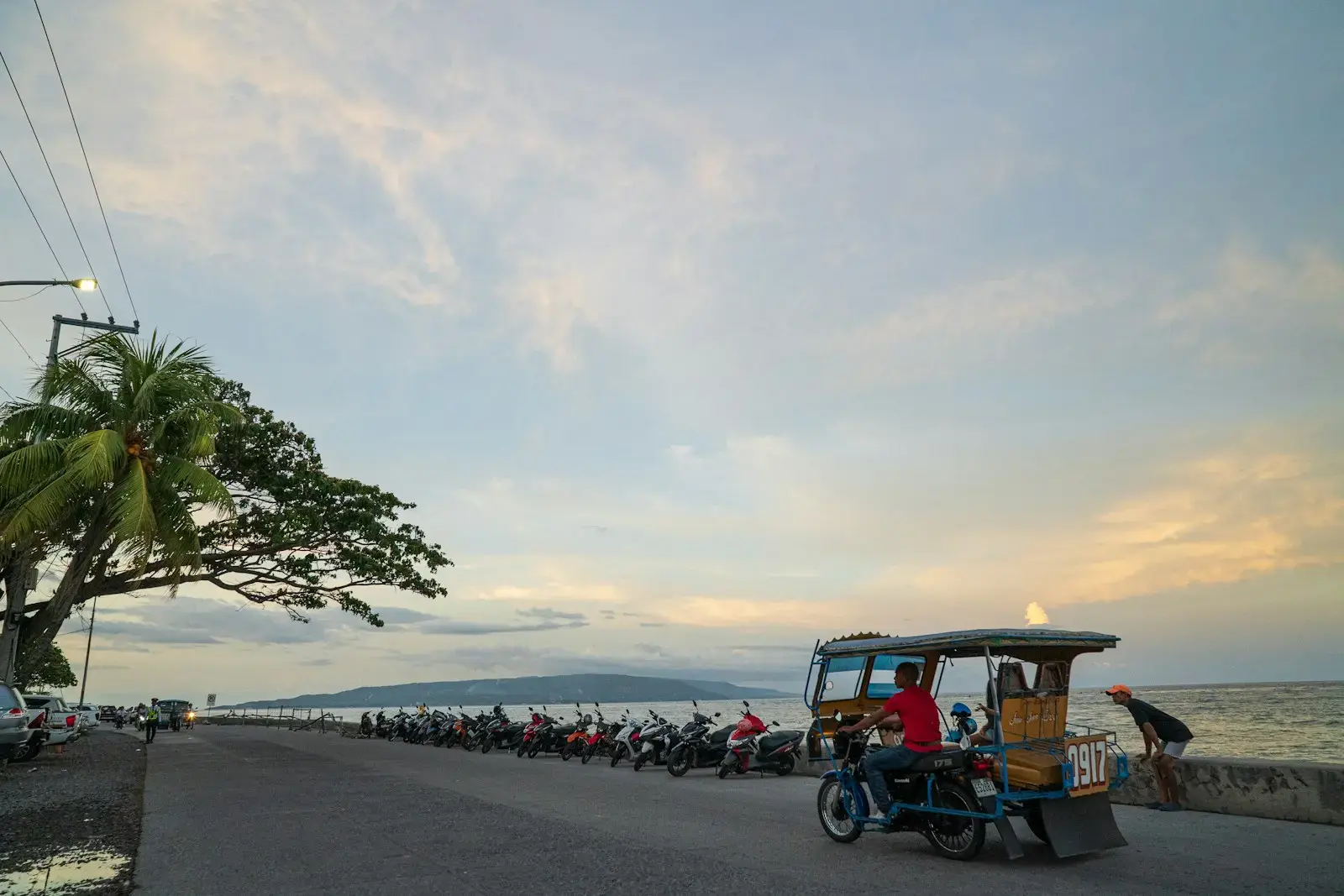 Photo by MacroLingo LLC Tricycle and parked motorcycles by the sea at sunset.