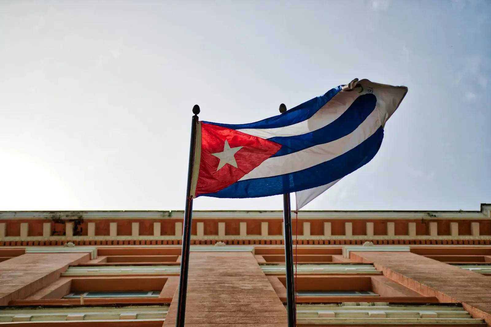 Photo by Matthias Oben Cuban flag waving against a historic building in Havana, capturing national pride and architectural beauty.