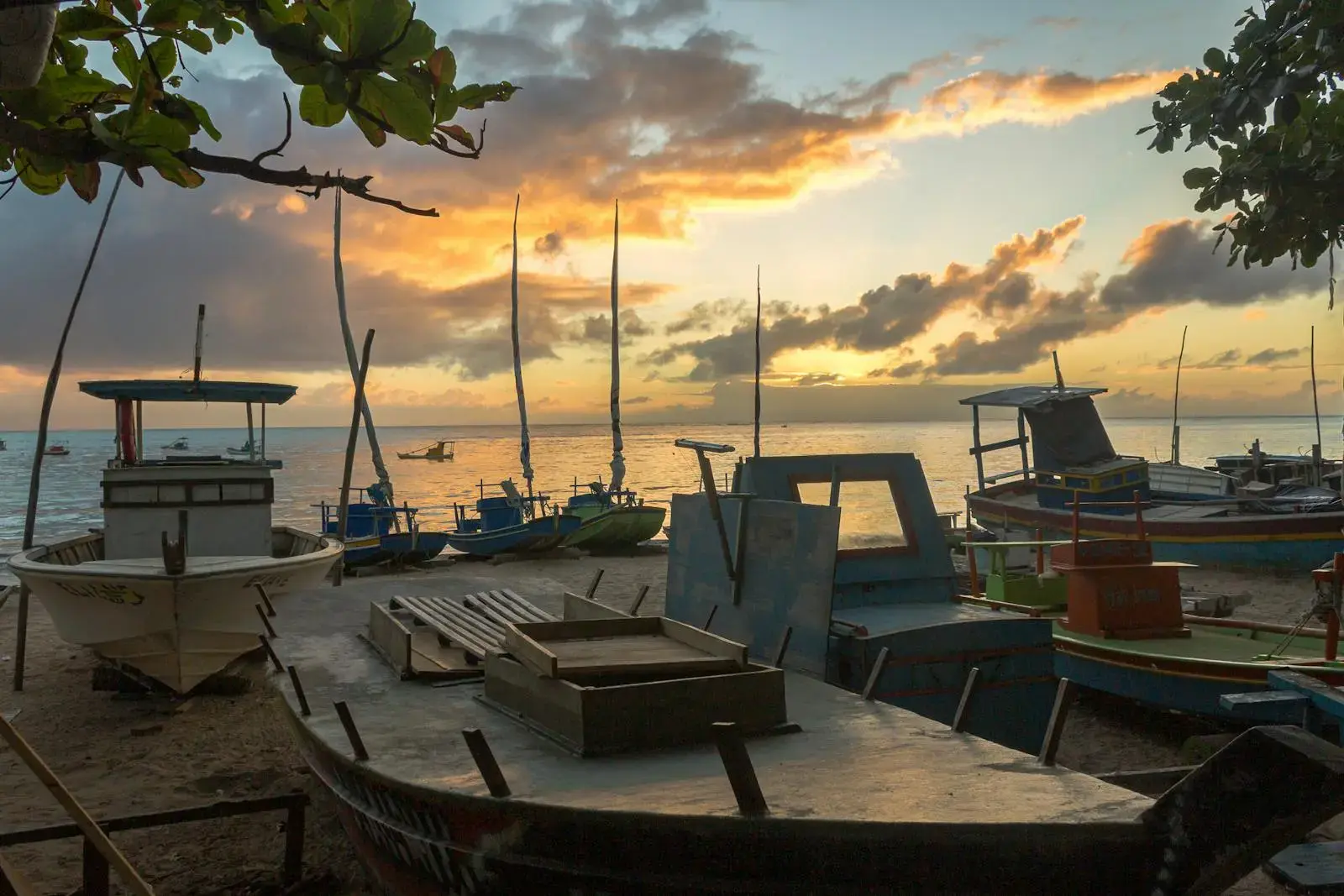 Photo by Daniel Guimarães Fishing boats on a sandy shore at sunset, with vibrant skies and calm sea.