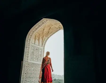 A woman in a traditional saree stands in a grand, ornate doorway with intricate patterns.