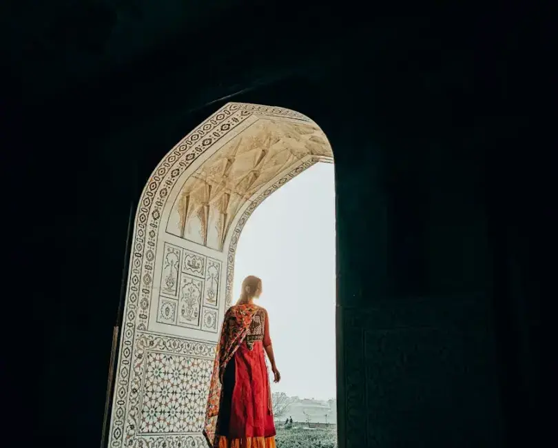 A woman in a traditional saree stands in a grand, ornate doorway with intricate patterns.