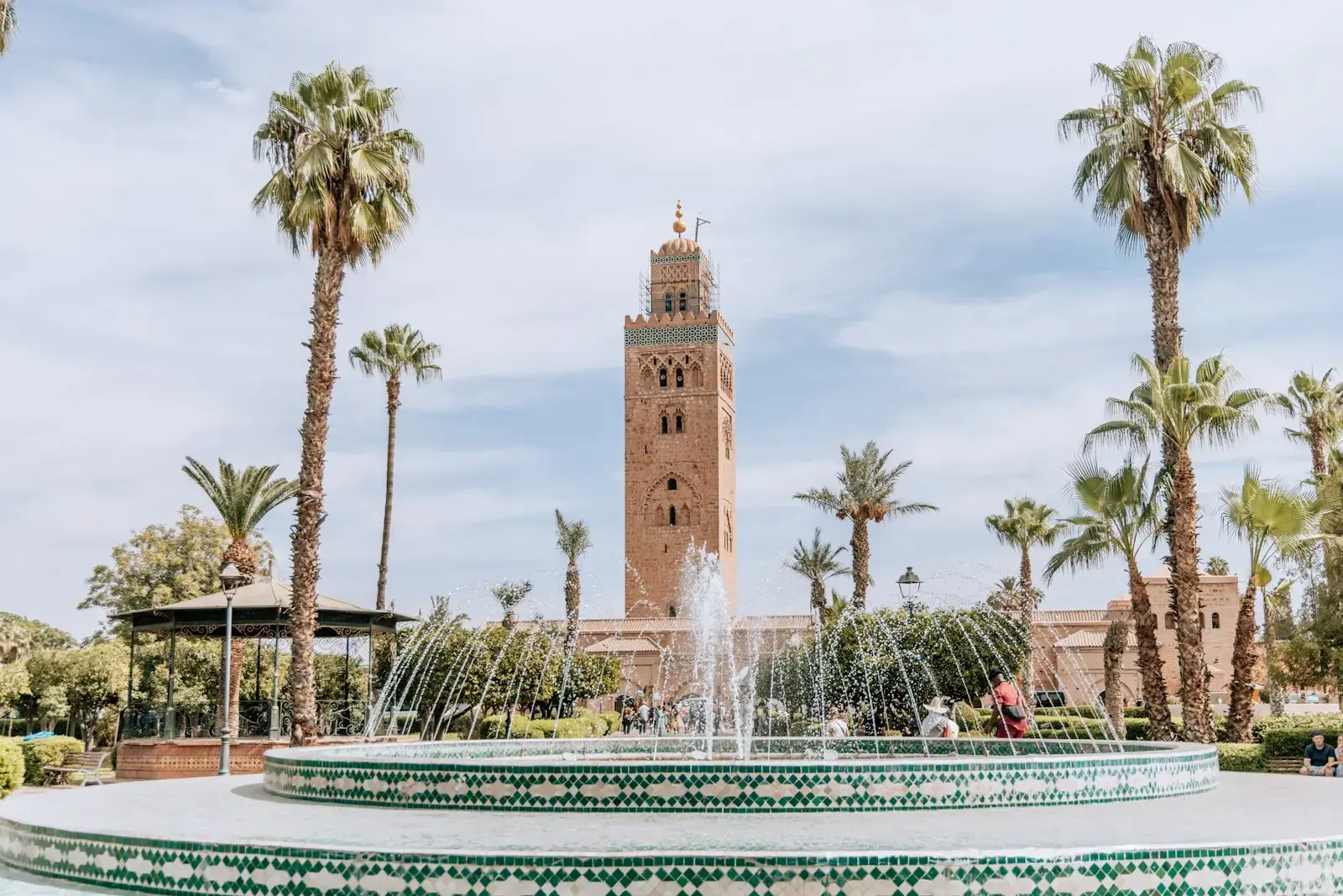 A fountain in front of a tall minaret tower.
