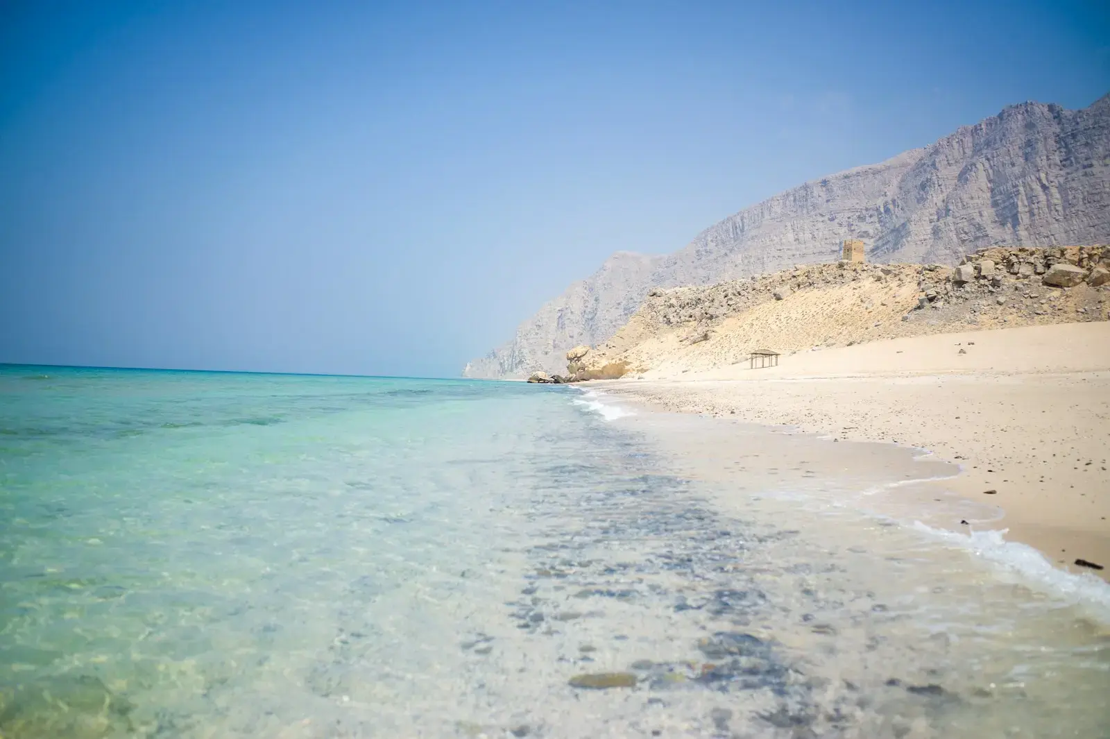 Photo by Julius Yls a sandy beach with clear blue water and mountains in the background