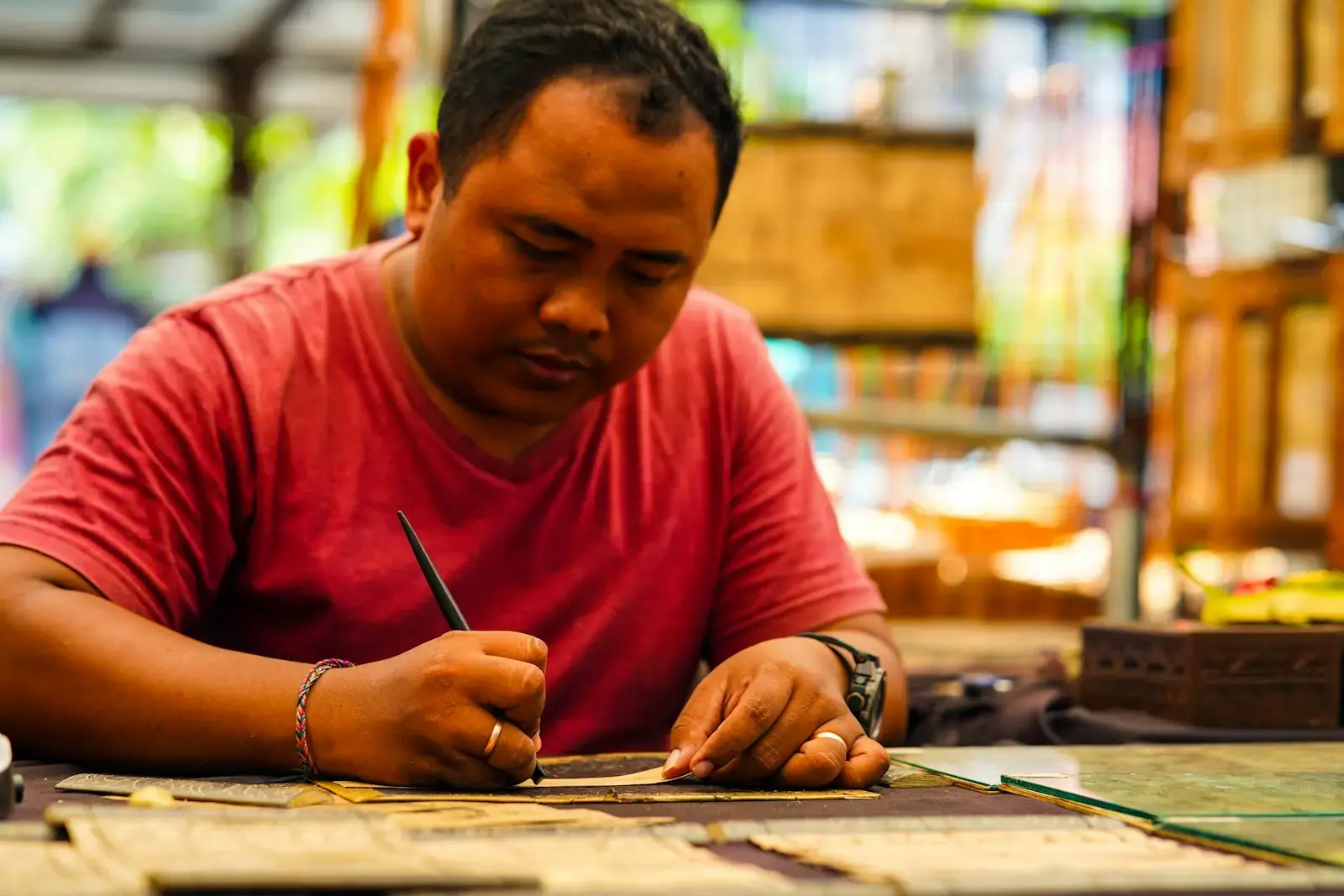 man in red long sleeve shirt writing on brown wooden table