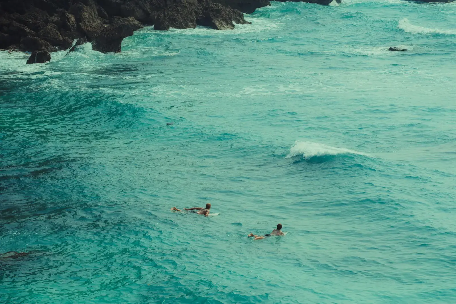 Photo by Matthew Stephenson Surfers are paddling in the turquoise ocean.