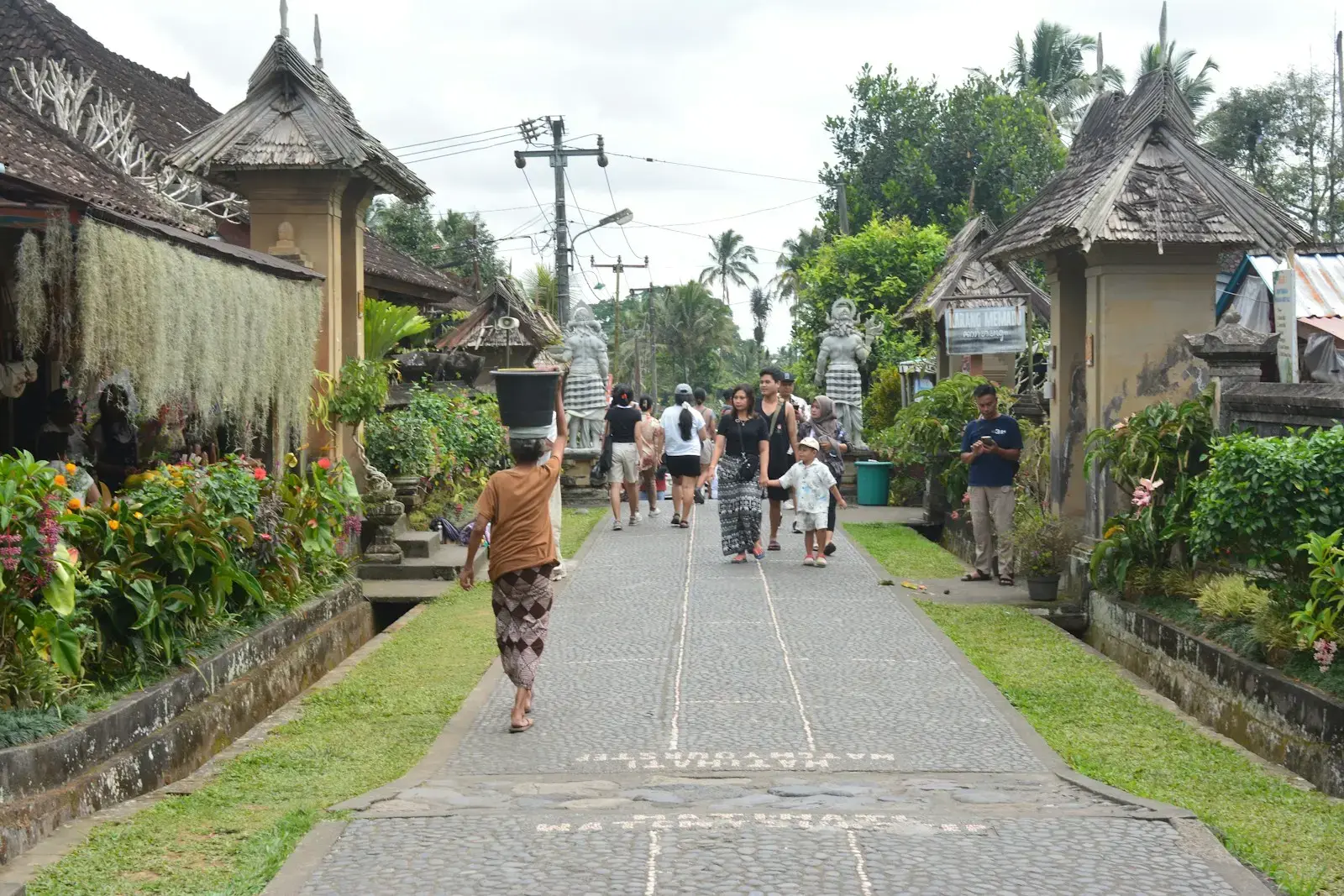 People walking down a village path with traditional buildings.