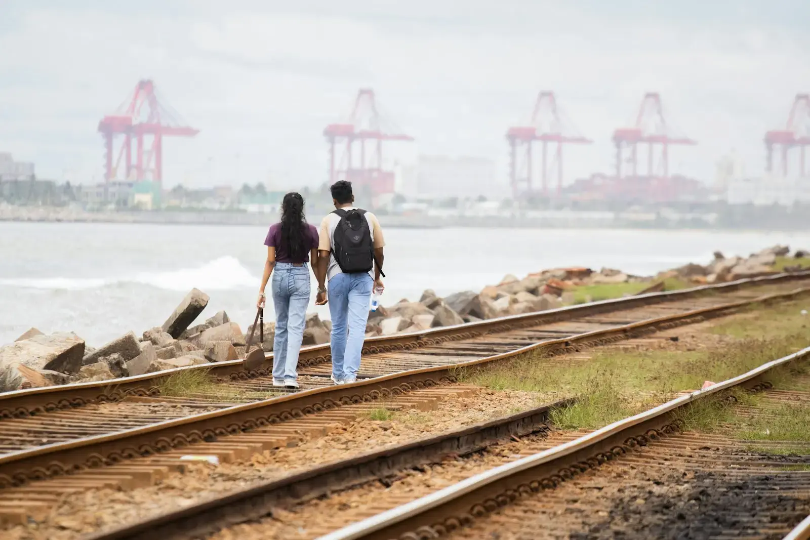A couple walks along train tracks near the ocean.