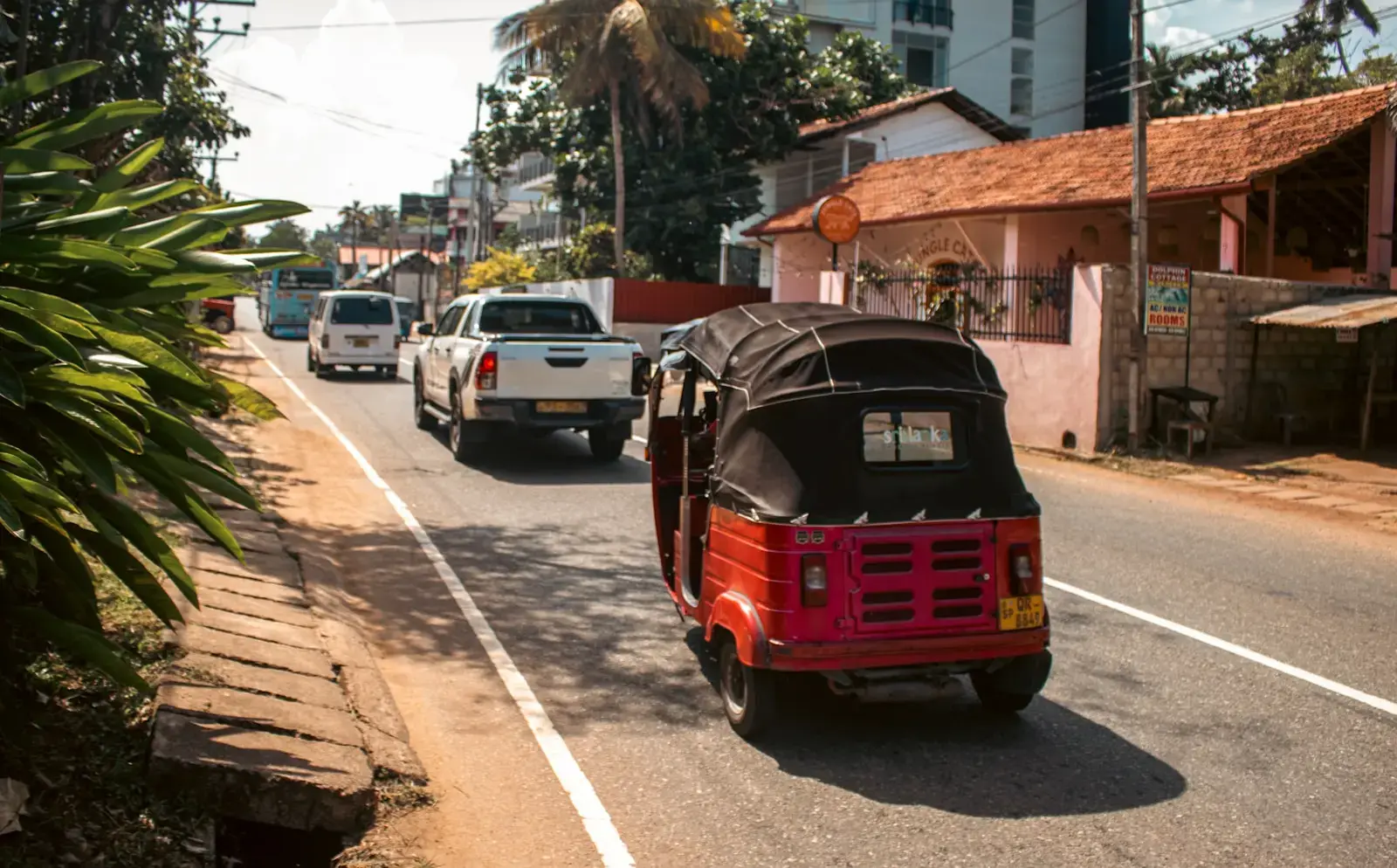 A red tuk-tuk drives down a sunny street.