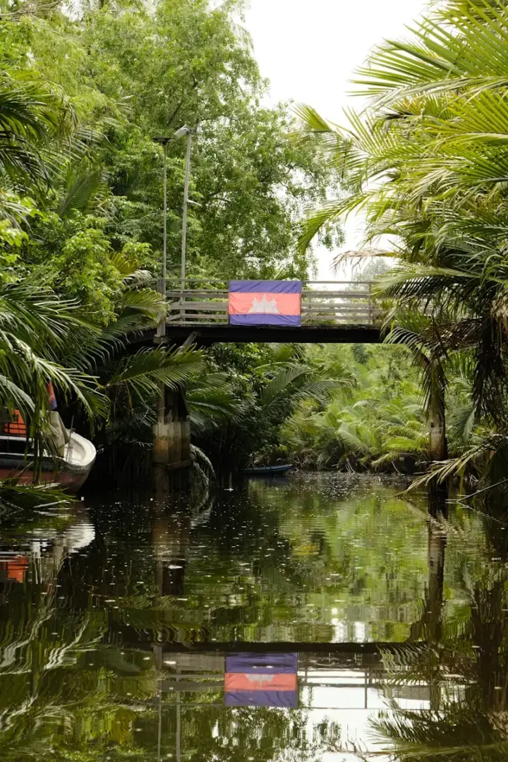 Photo by Siborey Sean A bridge over a body of water surrounded by trees