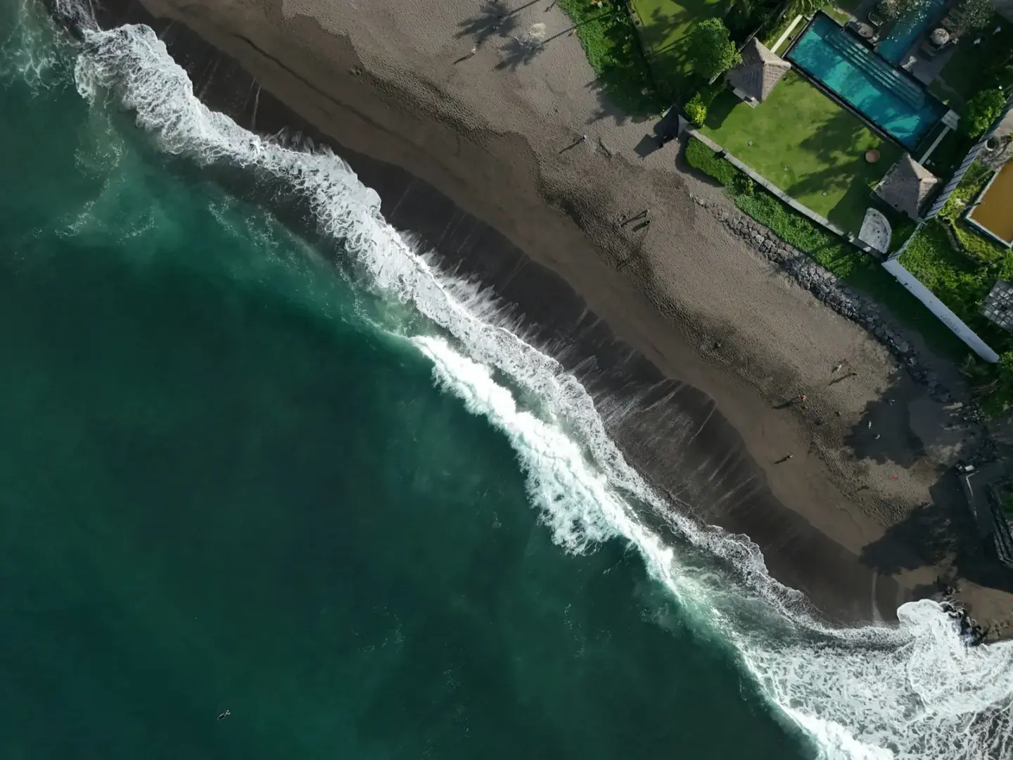 Waves crash on the beach near a luxurious villa.