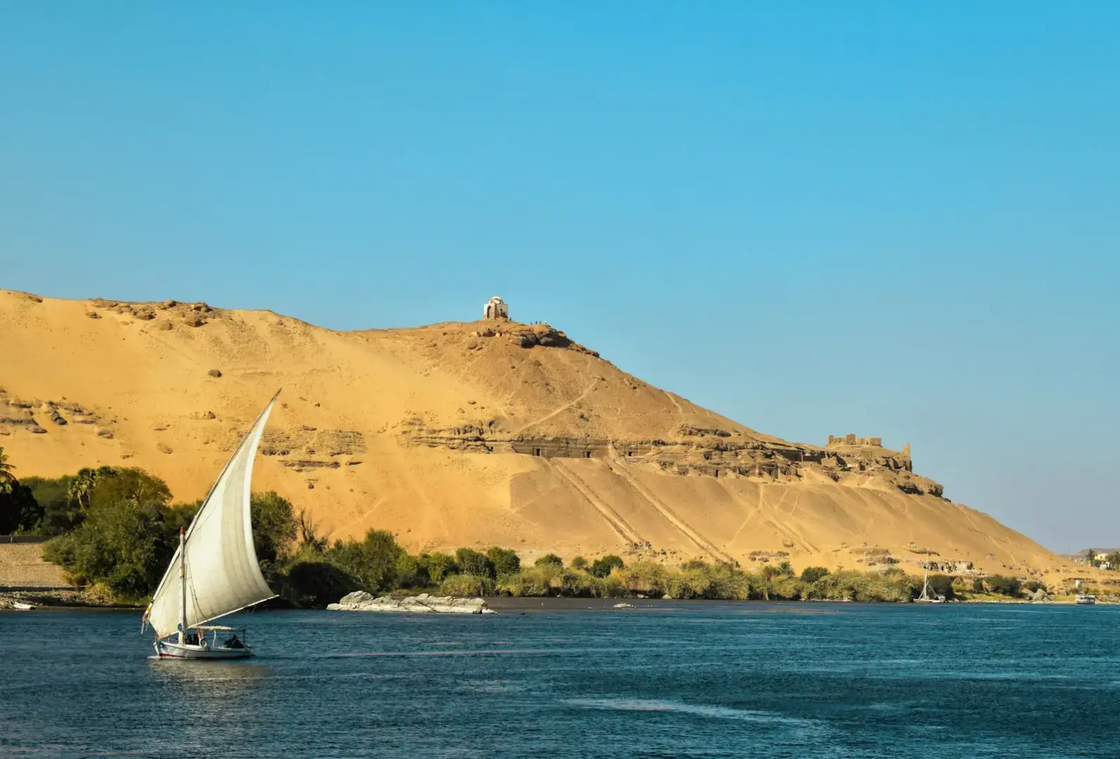 Photo by Xiaoqian Shen A sailboat glides on the nile river with desert hills.