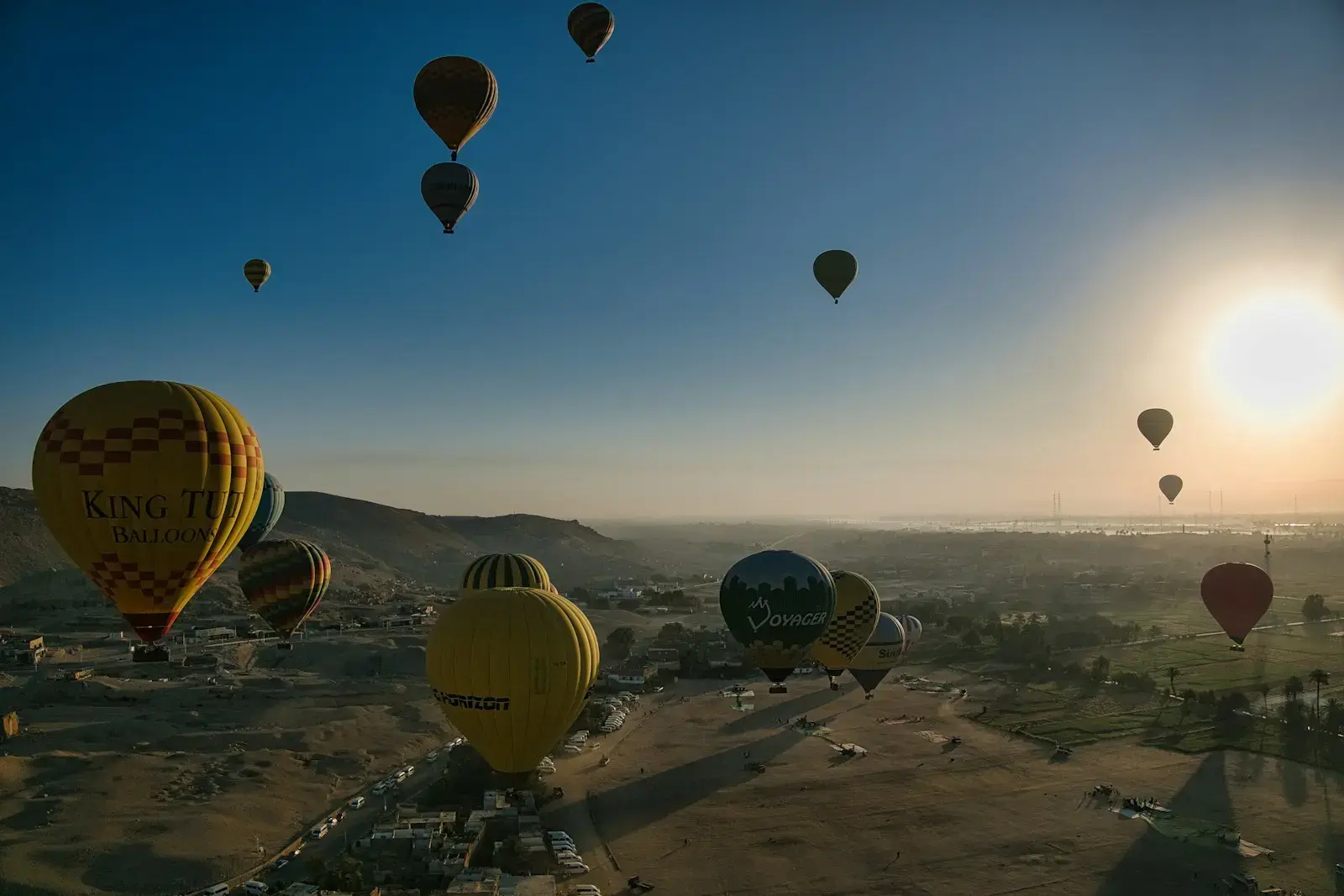 Hot air balloons ascend over a desert landscape at sunrise.