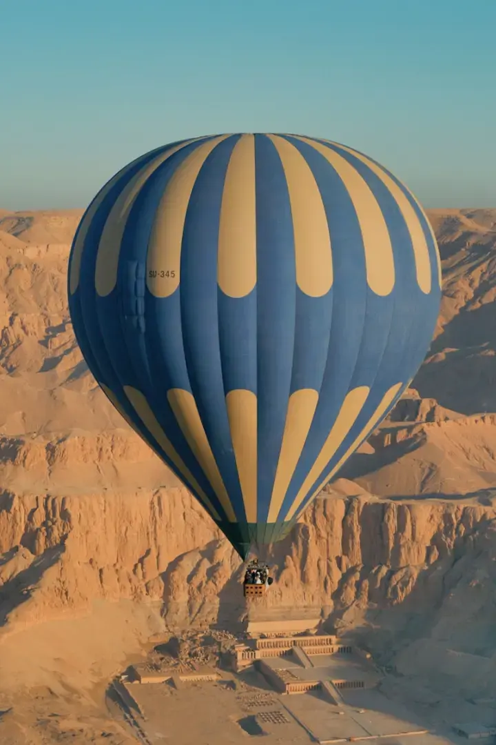 Photo by Filip Crantz Blue and yellow striped hot air balloon over ancient ruins.