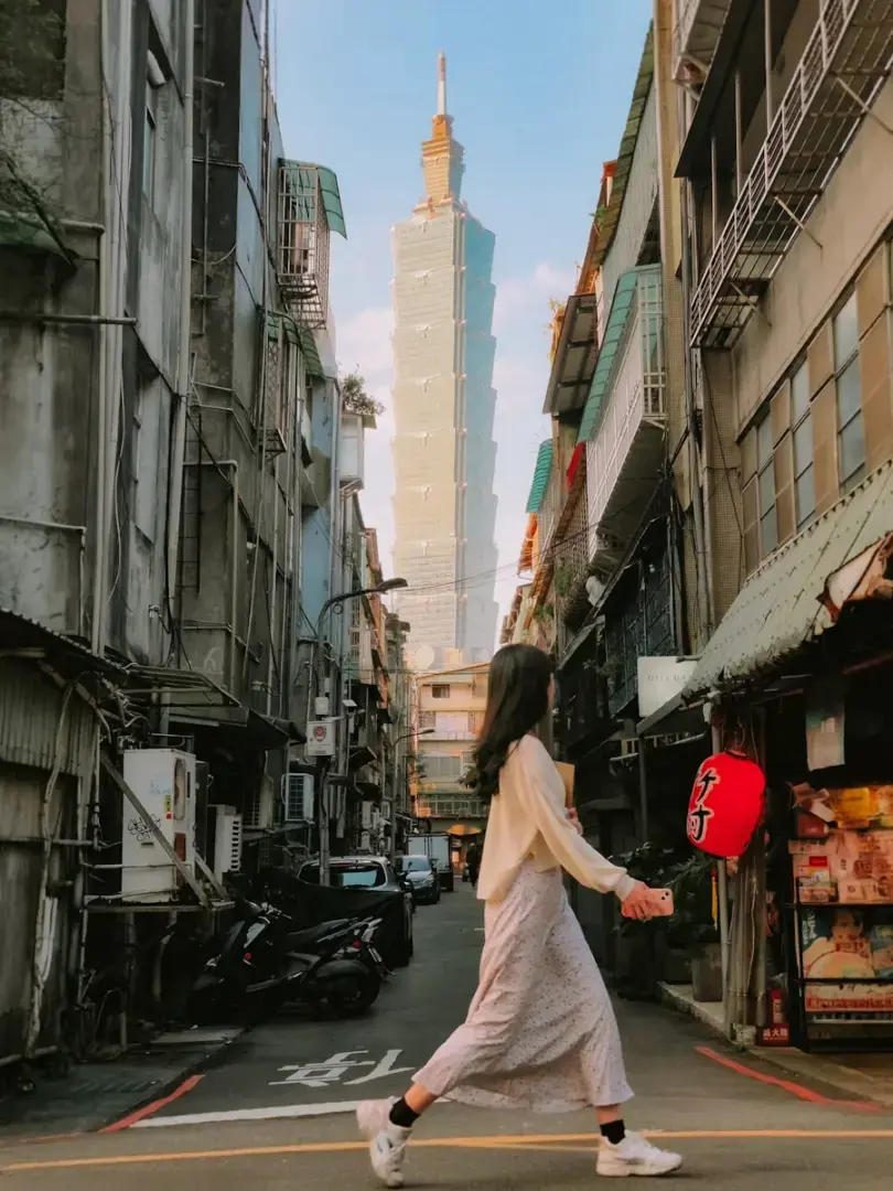 Woman walks down a narrow street towards taipei 101.
