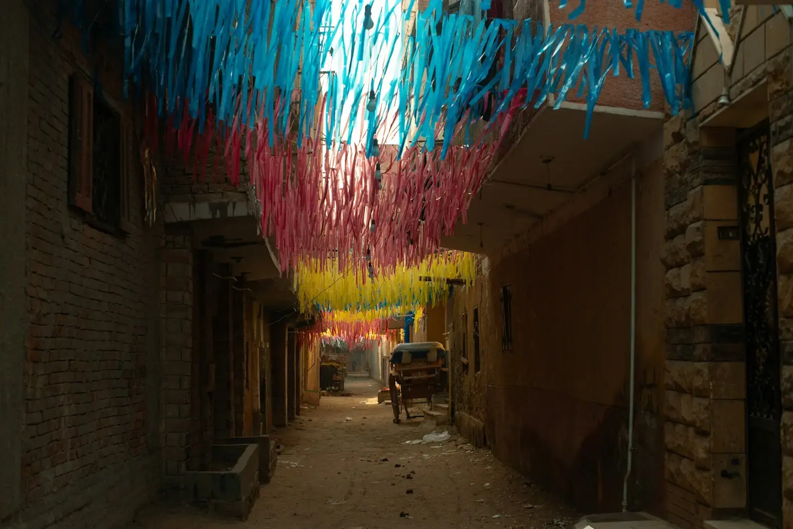 Colorful streamers hang over a narrow street with a vehicle.