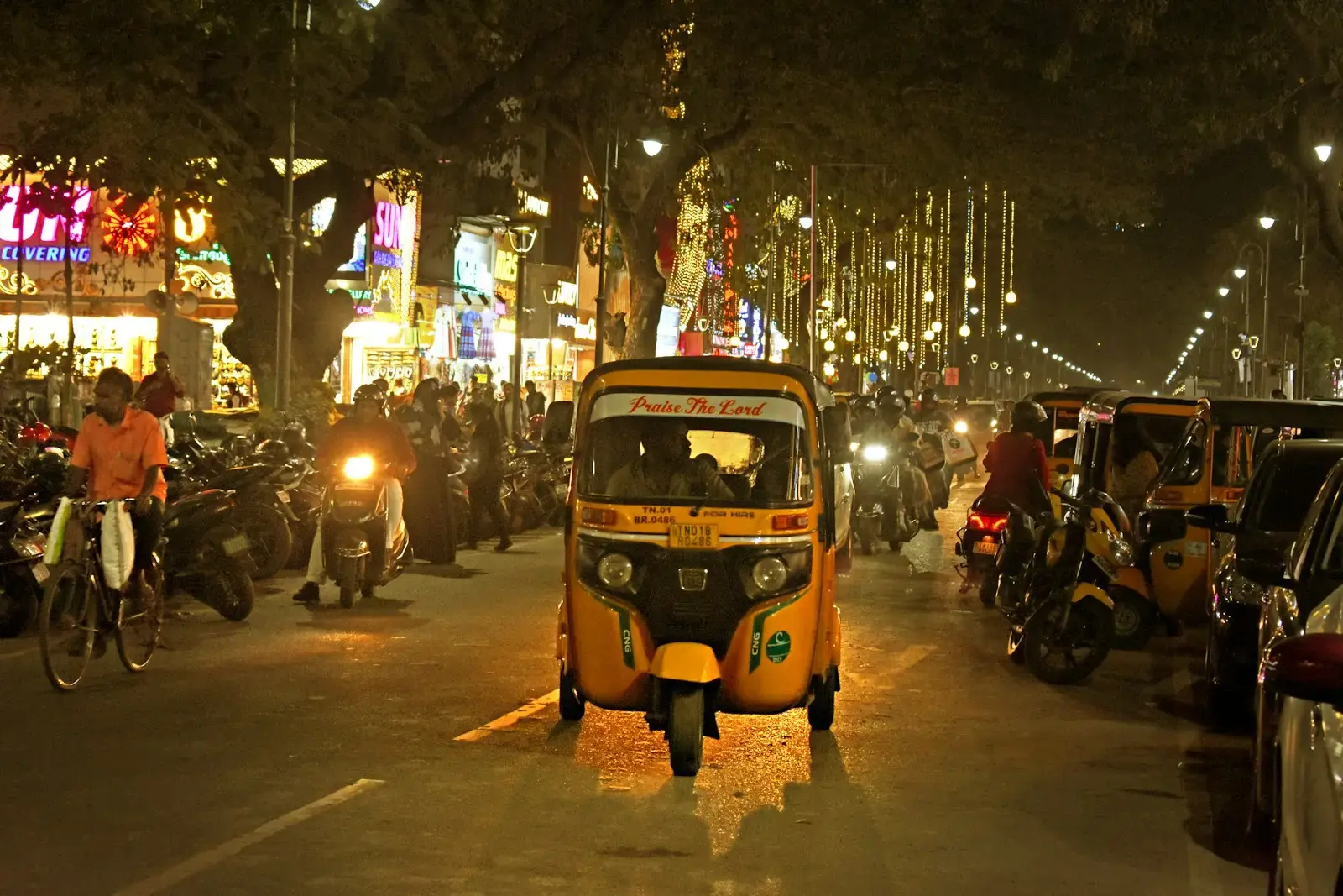 A yellow rickshaw drives through a busy street at night.