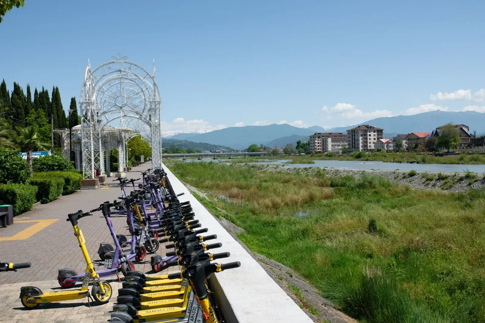 Photo by Oleksiy Yeshtokyn,🌻🇺🇦🌻 Electric scooters lined up on a riverside walkway under a clear spring sky.