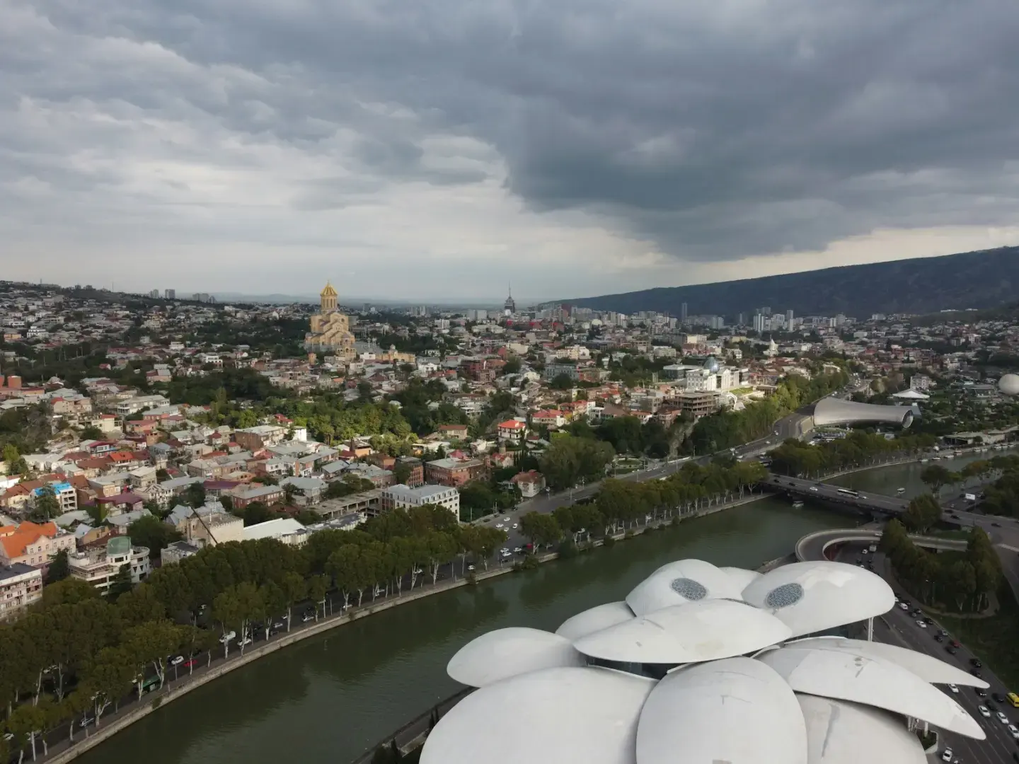 Photo by Mikheil Kuzmidi City panorama with a river, modern architecture, and cloudy sky.