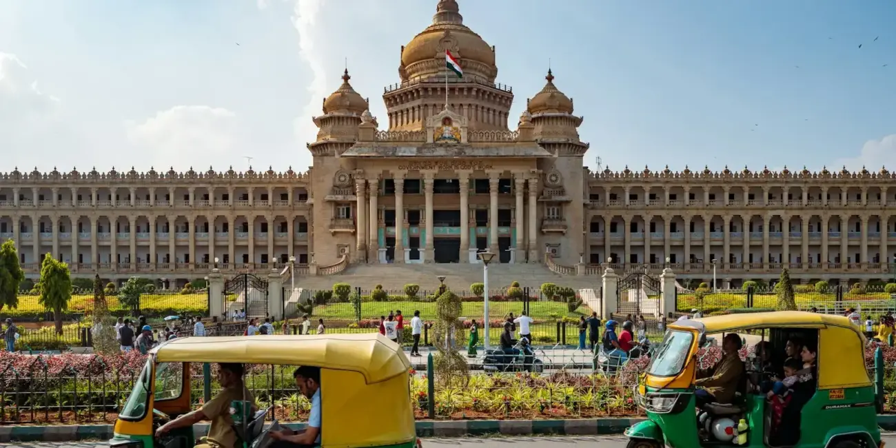 Tuk-tuks drive past a grand government building.
