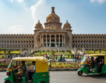 Tuk-tuks drive past a grand government building.