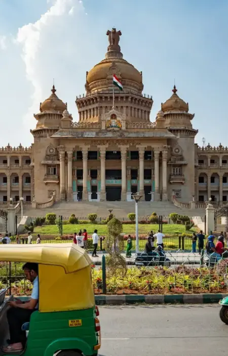 Tuk-tuks drive past a grand government building.