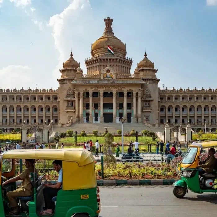 Tuk-tuks drive past a grand government building.