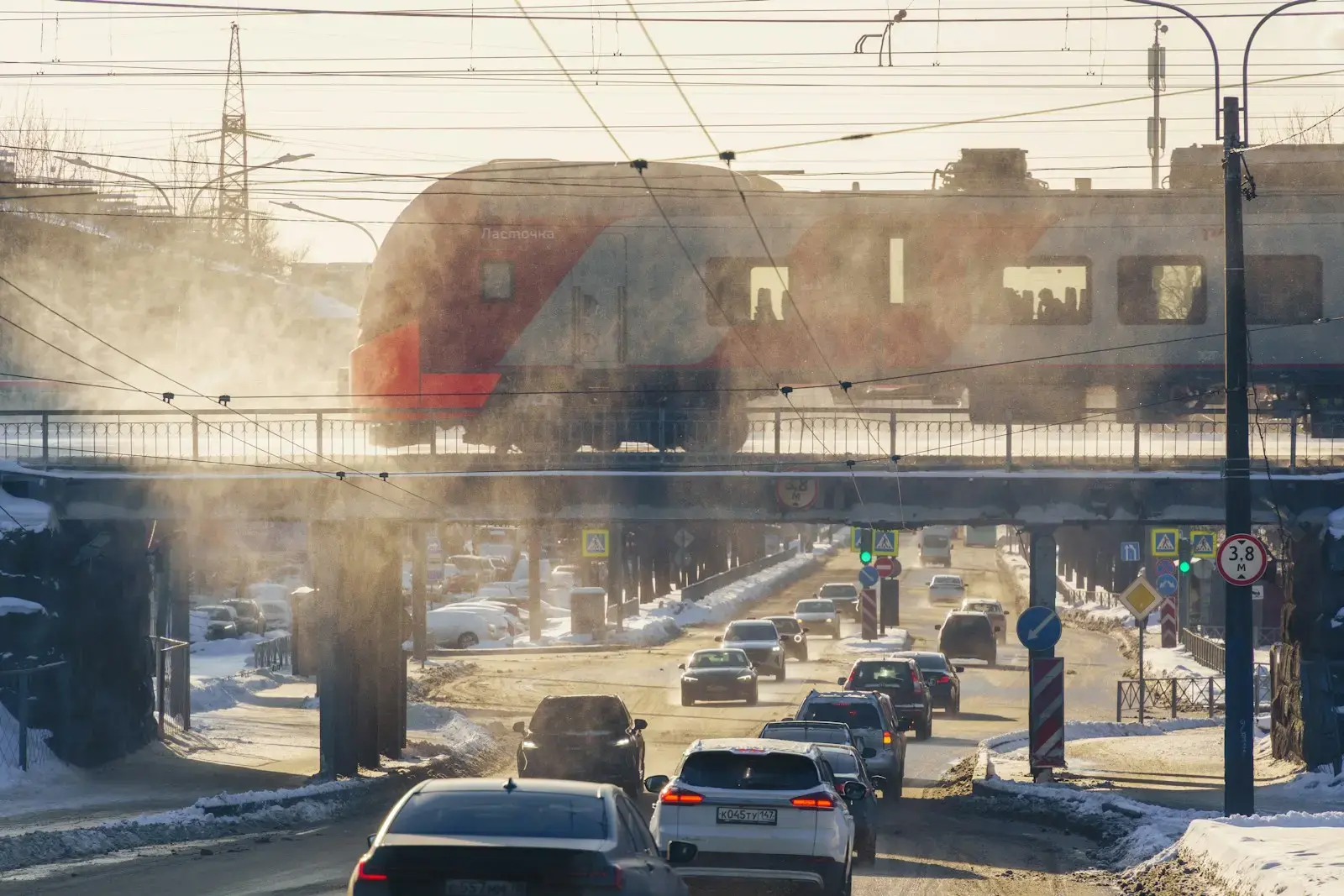Photo by Red Shuheart Train on bridge over road with cars in winter sun.