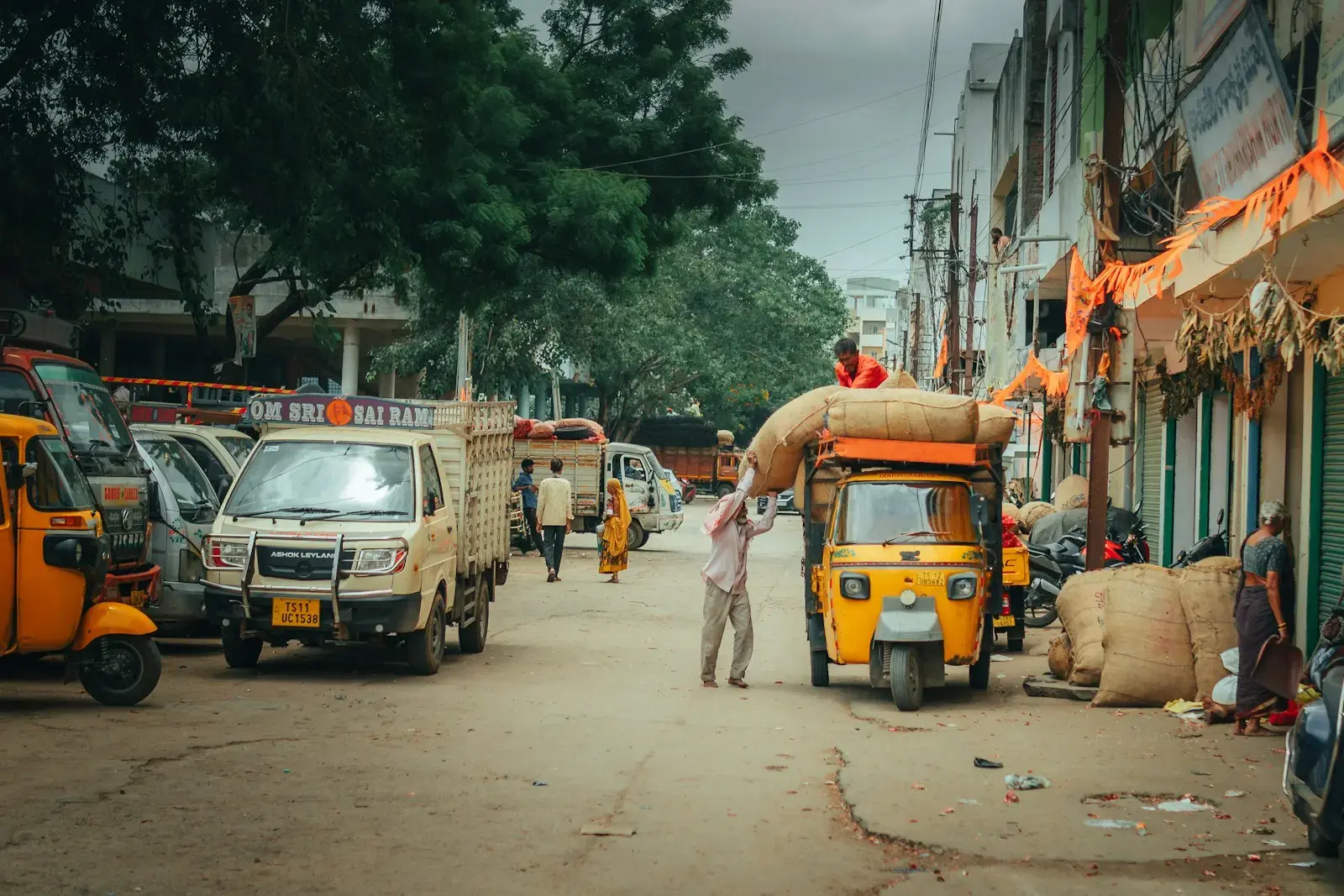 People load goods onto a tuk-tuk on a street.
