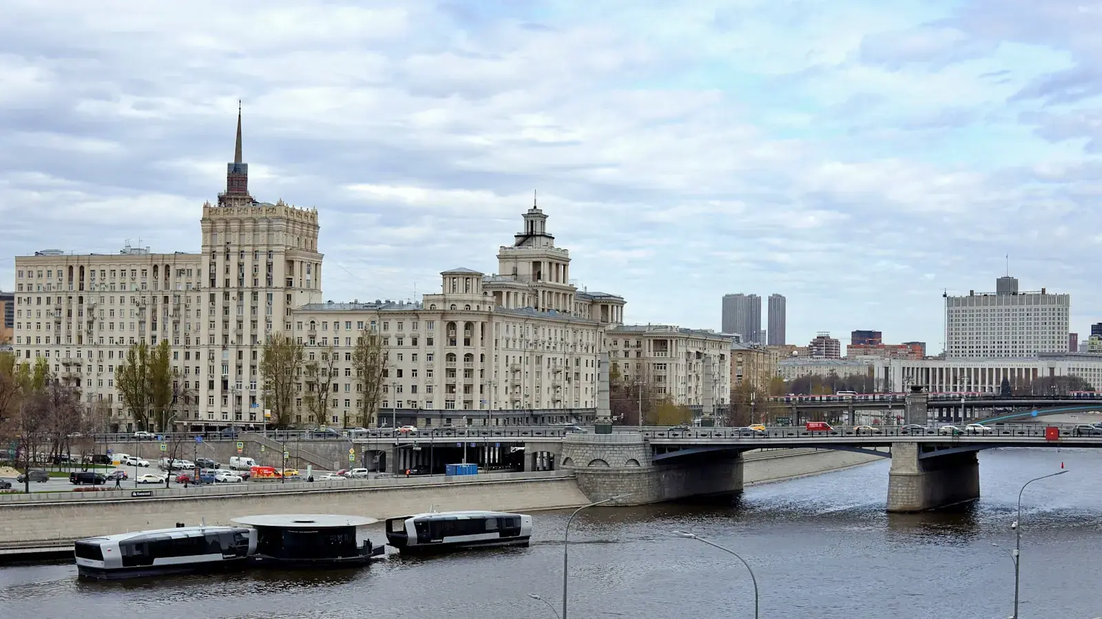 Photo by Murat Ts. Large buildings line a river with a bridge and boats.