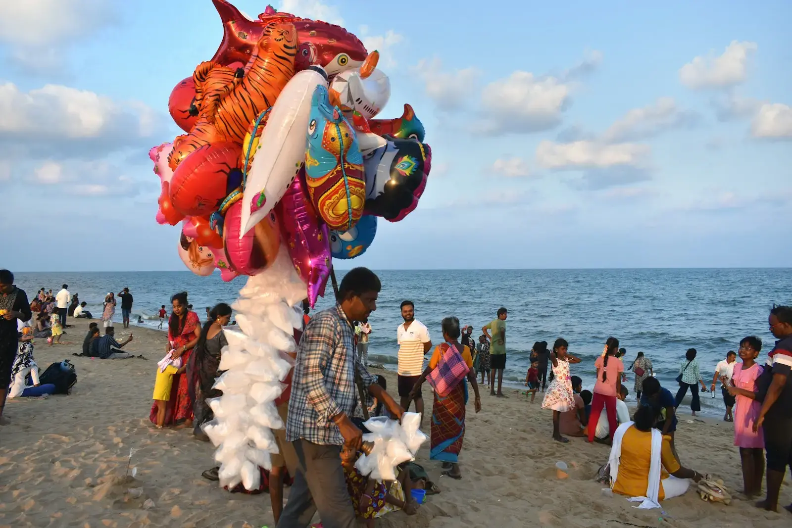 Man selling balloons on a crowded beach with ocean background
