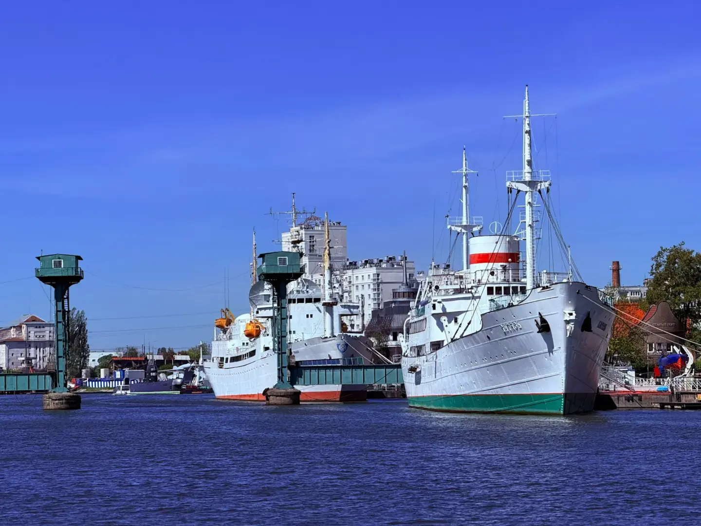 Photo by Ronin Two ships are docked in a harbor with buildings.